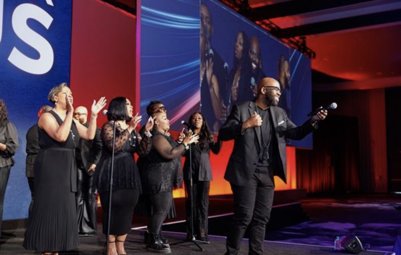 Vocal group performing on a lit stage with large video screens