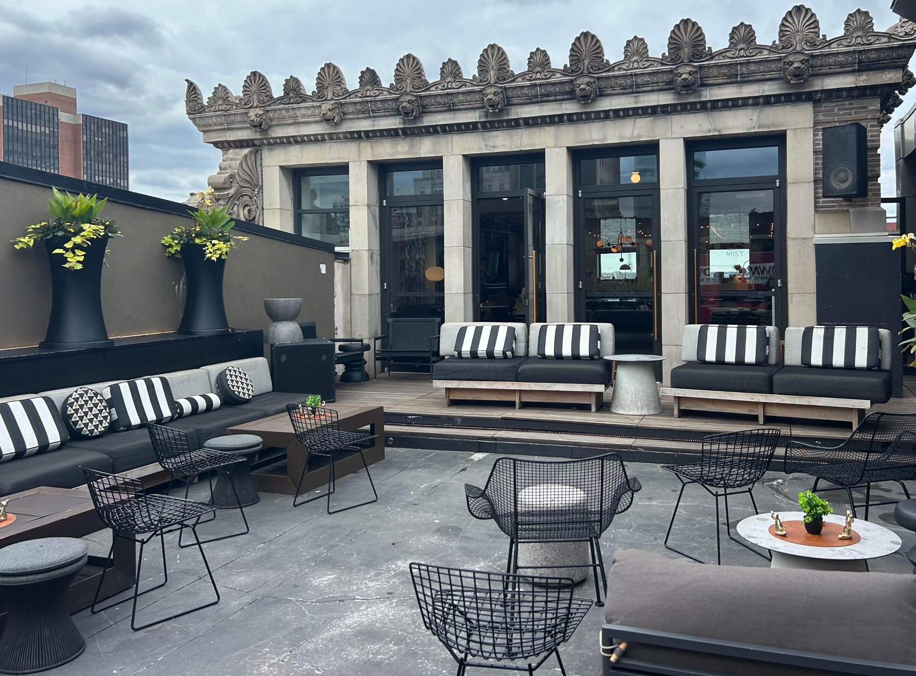 Rooftop lounge with striped cushions and wire chairs below an ornate stone cornice